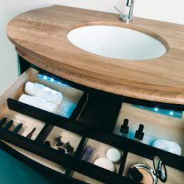 Baño oval con gavetas de madera lacada e iluminación interior con lavabo encastrado en encimera de madera